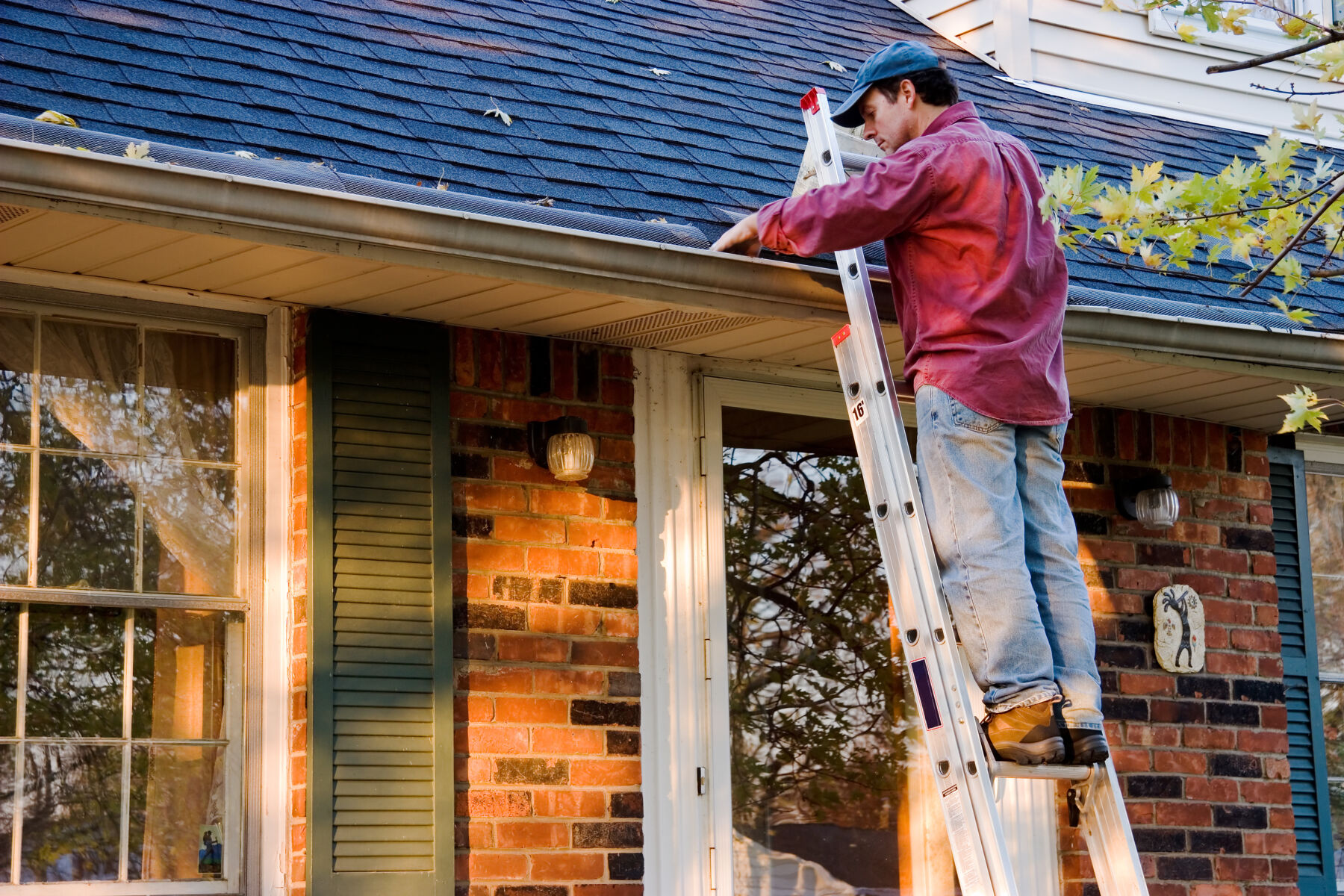 Man on ladder cleaning out leaves and debris from gutter