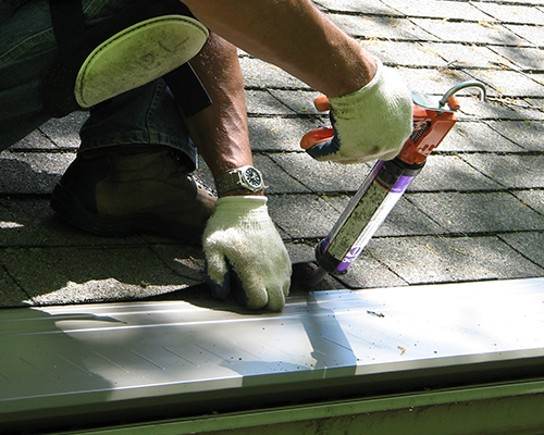 A roofing professional installing gutter topper on a home roof.
