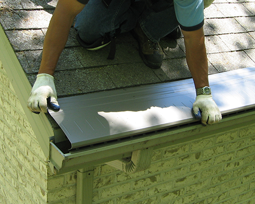 A roofer installs gutter topper over an existing roof on a home.