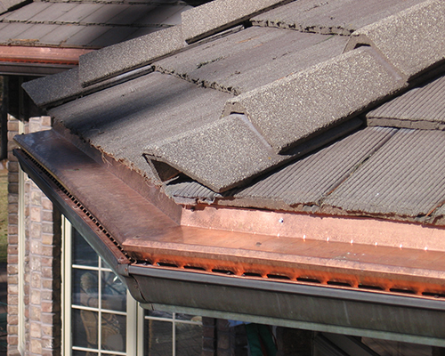 The edge of a home roof with gutters covered by Gutter Topper.