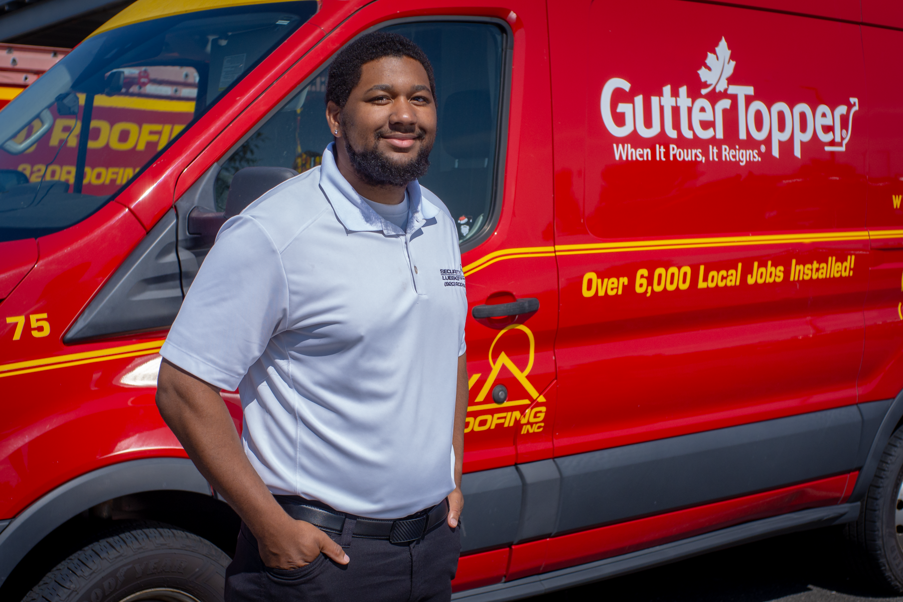 A man in a white polo shirt stands smiling in front of a red service van with "GutterTopper" and "Over 6,000 Local Jobs Installed!" written on the side.