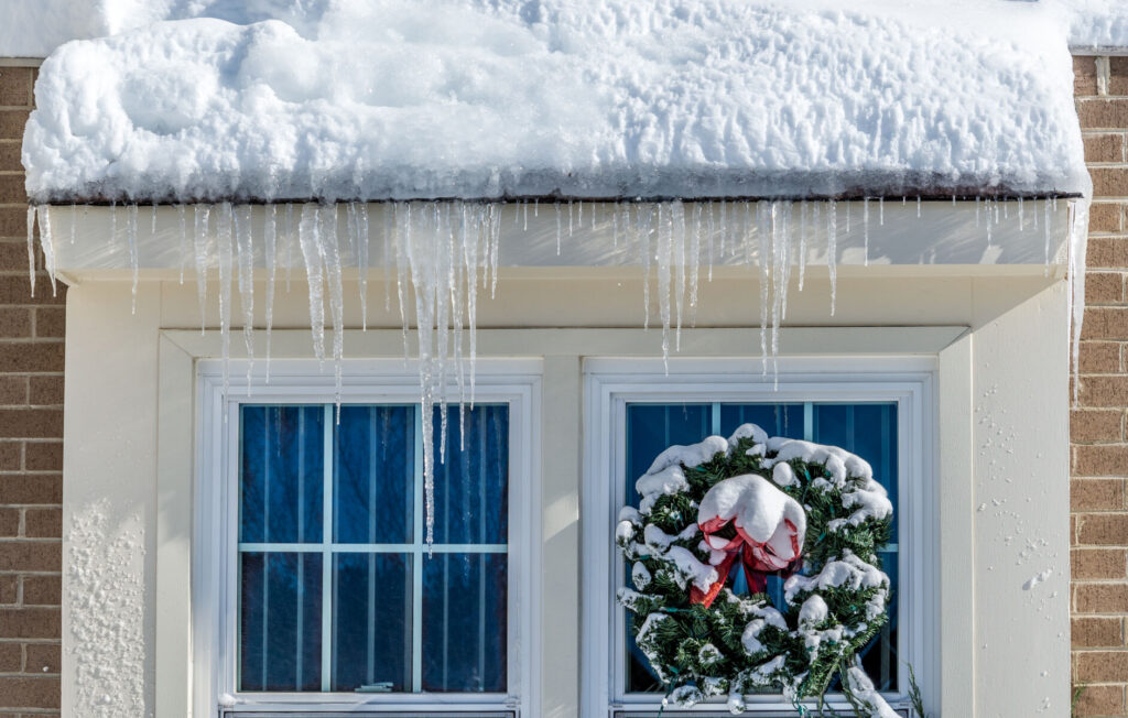 Wreath on window under snowy roof. winter roof maintenance tips.
