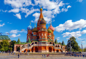 St. Basil's Cathedral, showcasing its vibrant, onion-shaped domes, stands majestically under a blue sky with white clouds. Located in Moscow's Red Square, this iconic wonder is a striking example of fascinating roofs around the world as people bustle below, enjoying the captivating view.